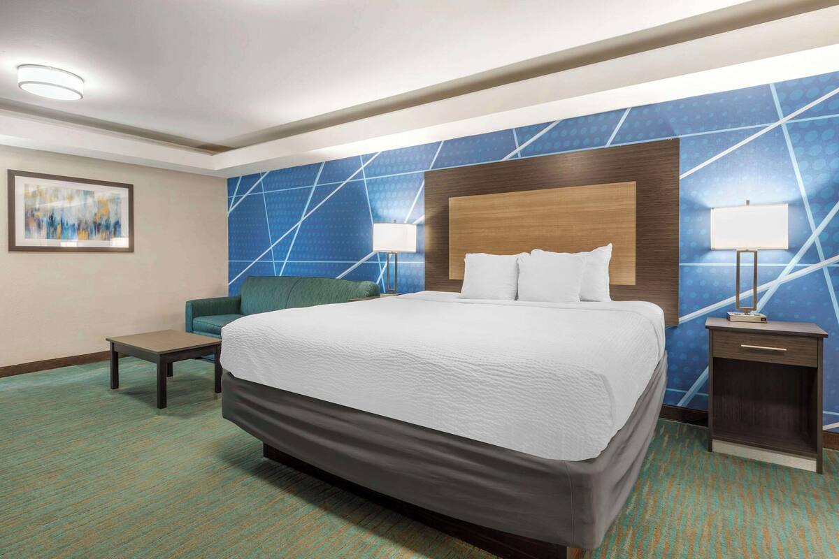 A hotel room with a large bed, two bedside tables, a chair, and a wall with a geometric pattern.