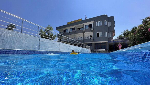 Una piscina con agua azul cristalina, un flotador amarillo y un edificio con balcones al fondo.