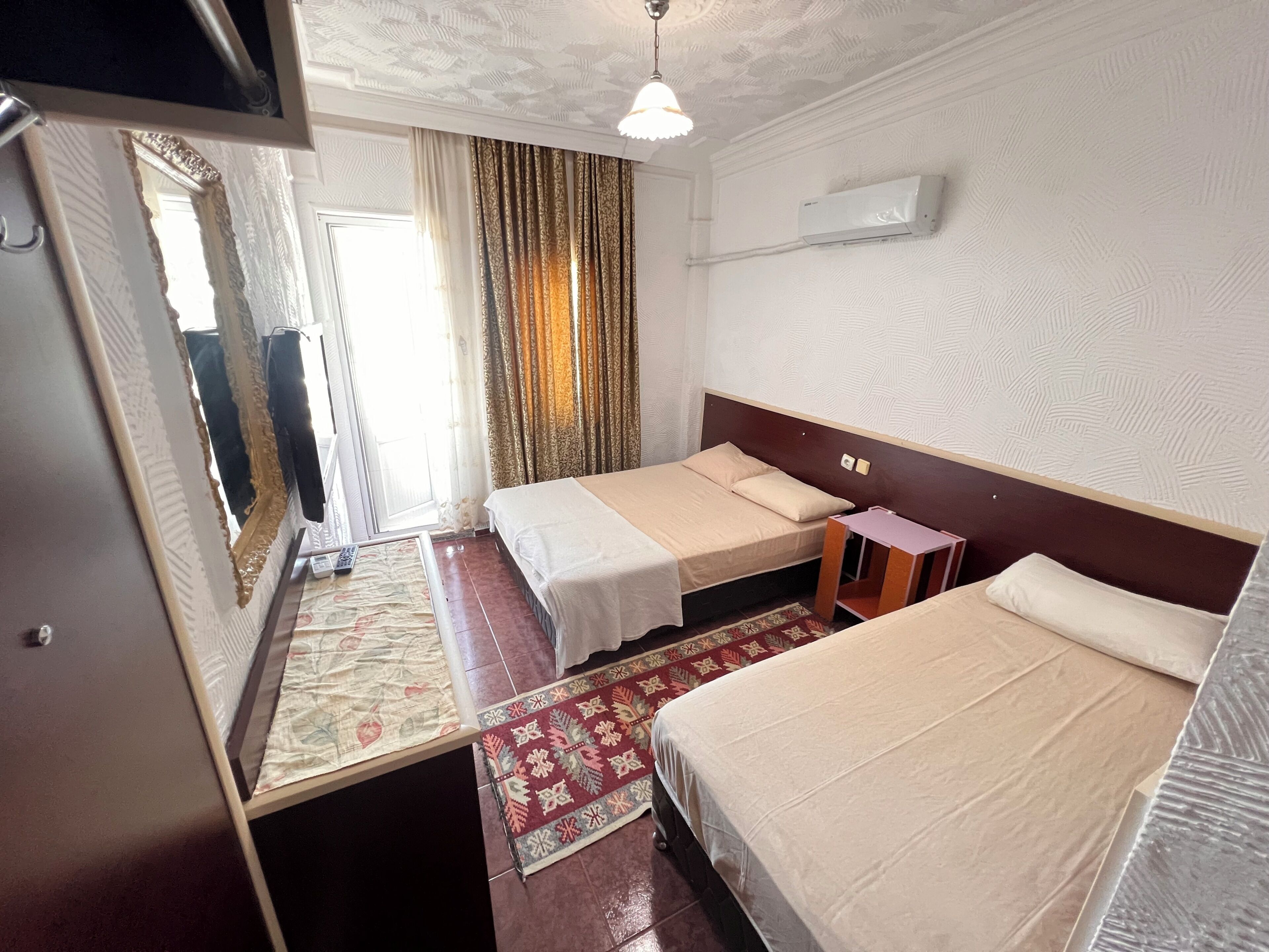 A hotel room with two beds, a large mirror, a ceiling fan, and a window with curtains.