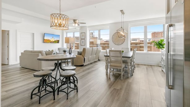 A spacious living area with a dining table, bar stools, and a large window offering a city view.