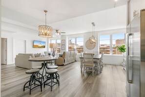 Uma sala de estar ampla com mesa de jantar, banquetas de bar e uma grande janela com vista para a cidade.