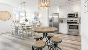 A modern kitchen with white cabinets, stainless steel appliances, and a round wooden dining table with stools.