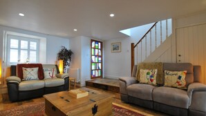 A living room with two sofas, a wooden coffee table, a staircase, and a stained glass window. - Aqua Vista- seafront cottage, Cellardyke (Anstruther)
