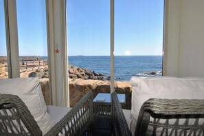 A balcony with wicker furniture, a view of the sea, and a rocky shoreline. - Aqua Vista- seafront cottage, Cellardyke (Anstruther)