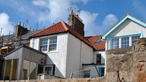 A stone wall with a staircase leading to a building with a red-tiled roof and a window with a blue frame. - Aqua Vista- seafront cottage, Cellardyke (Anstruther)