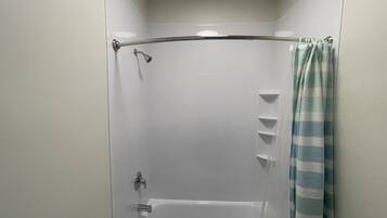 Una ducha con puerta de vidrio, un cabezal de ducha de mano y una cortina.