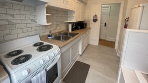 Una cocina compacta con armarios blancos, estufa, pileta y microondas.