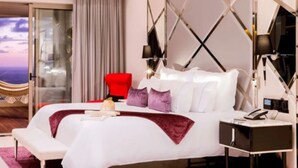 Habitación de hotel moderna con una cama grande, un sillón rojo, una hamaca y vistas a la ciudad.