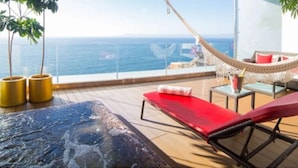 Un balcón con jacuzzi, una hamaca y vistas al océano.