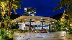 Un hotel moderno con estructura de techo curva, plantas de interior y vista a un rascacielos al fondo.