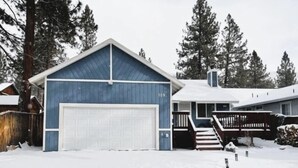 A two-story house with a blue garage and a white front door, surrounded by snow and trees. - Casa De Campo (Big Bear City)
