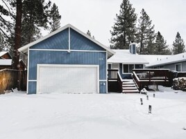 Una casa de dos pisos con un garaje azul y una puerta principal blanca, rodeada de nieve y árboles.