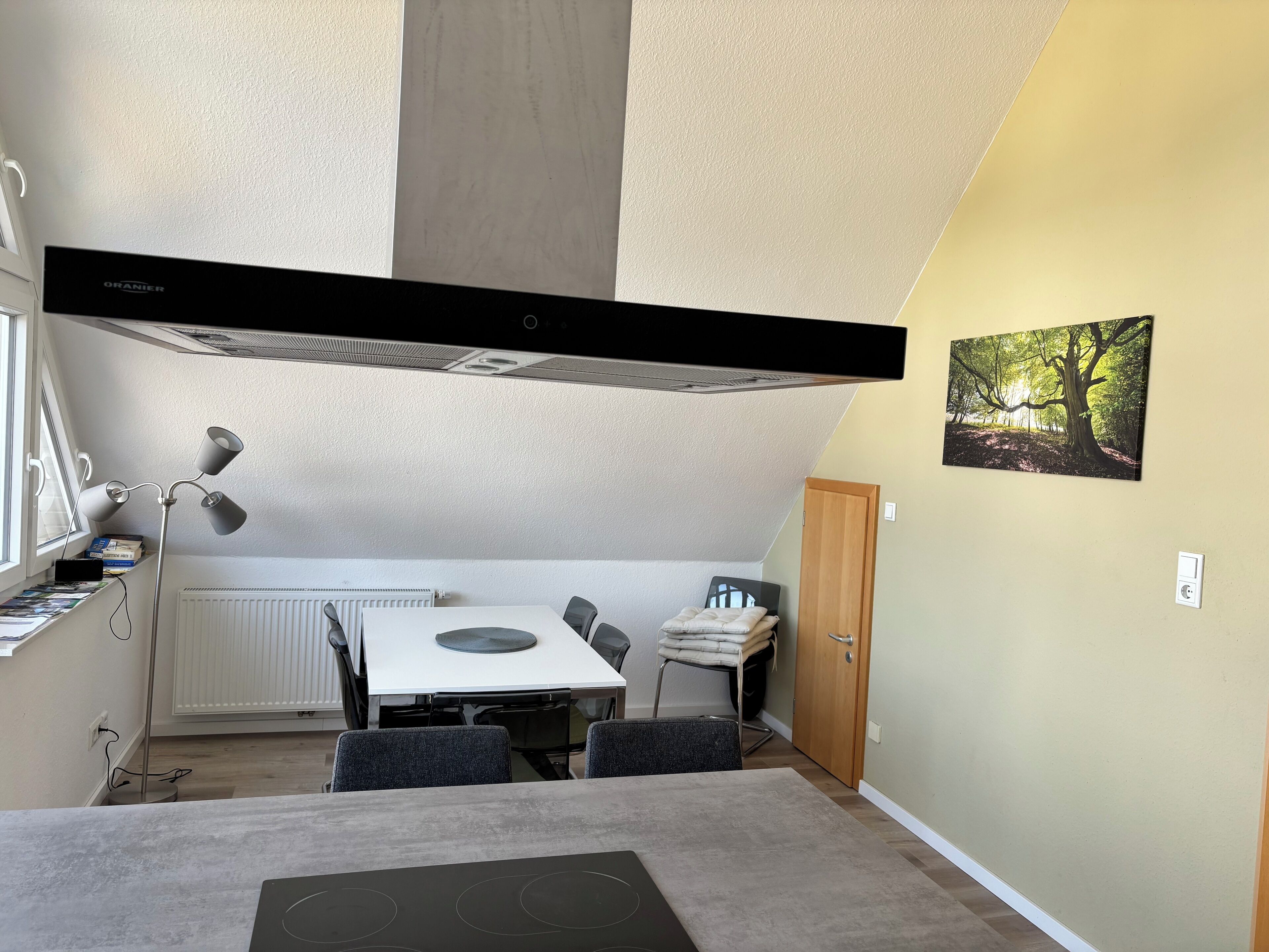 Un espace de vie compact comprenant une table à manger, des chaises, un radiateur, un lampadaire et un tableau accroché au mur.