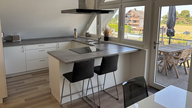 Une cuisine moderne dotée d’une grande fenêtre, d’une cuisinière encastrée et d’un coin bar avec deux tabourets.