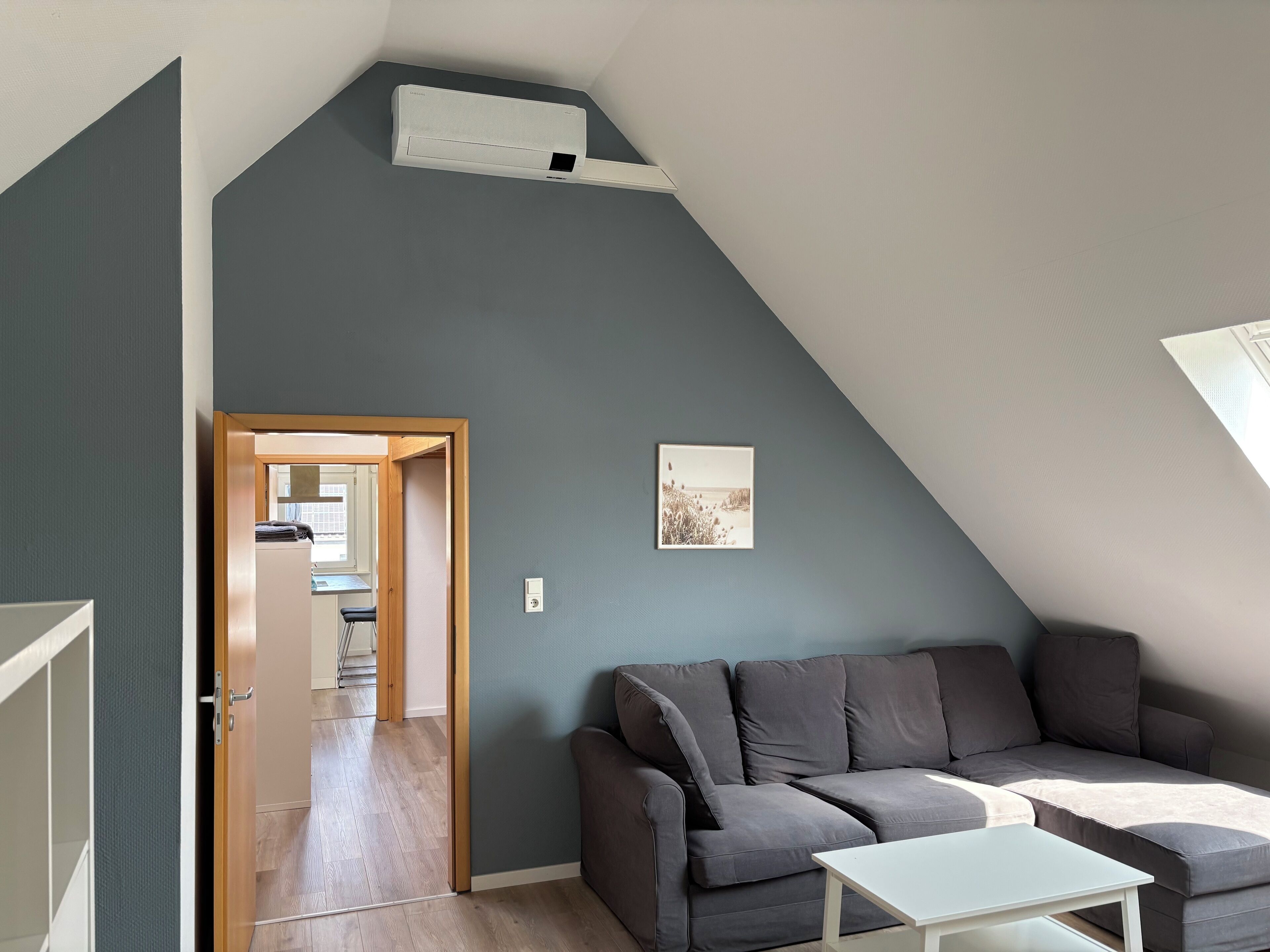 Un salon moderne avec un canapé gris, une table basse blanche et un climatiseur fixé au plafond.