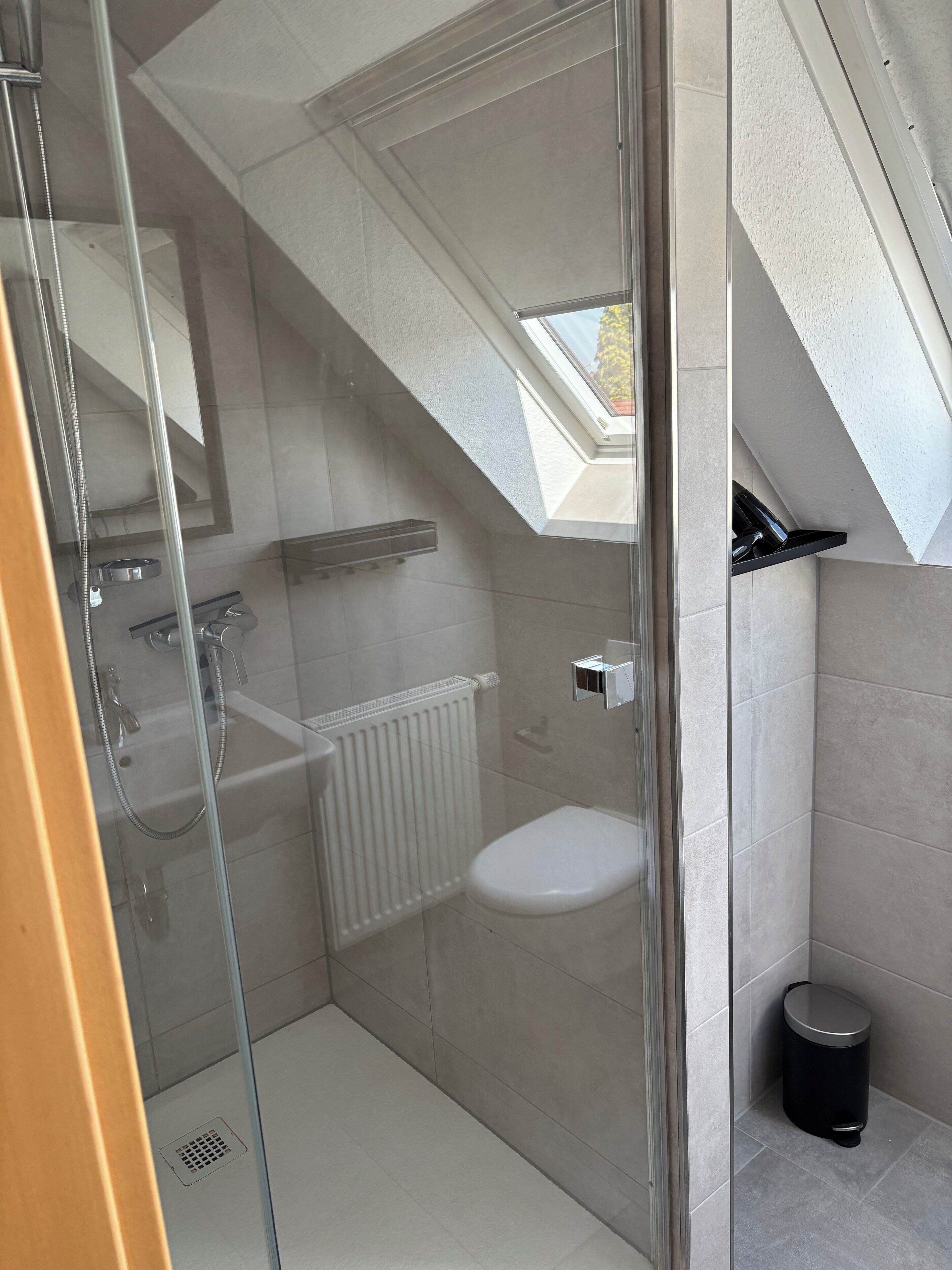Un bagno moderno con cabina doccia in vetro, un water bianco, un termosifone e un piccolo cestino.