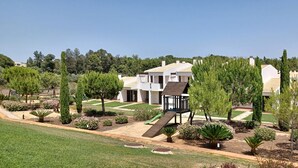Una villa moderna con un amplio patio, una terraza de madera y diversos jardines ajardinados.