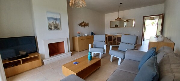 A living room with a TV, sofa, chairs, a coffee table, a fireplace, and a dining area.