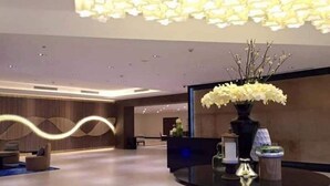 A modern lobby with a round table, a vase of white flowers, and a unique ceiling light fixture. - The Mactan Newtown (Lapu-Lapu)
