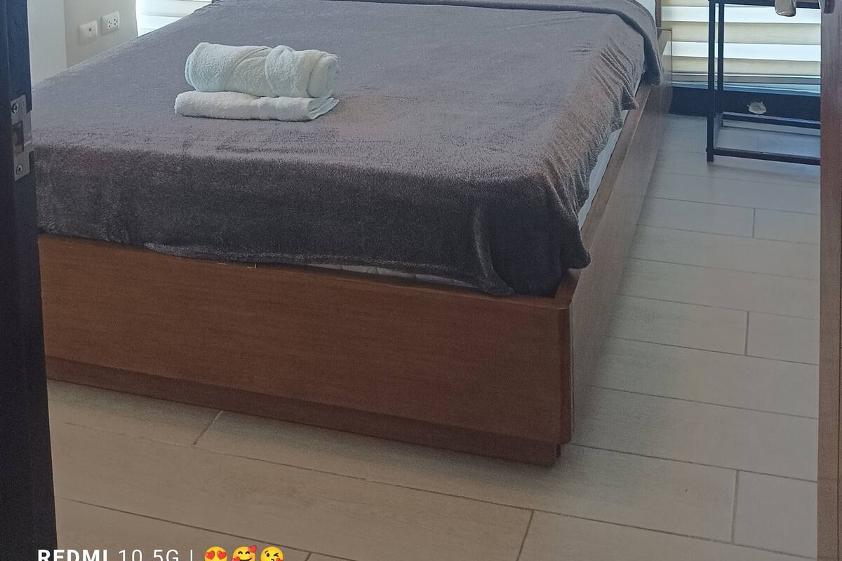 A bedroom with a bed, two bedside tables, and a window with blinds.