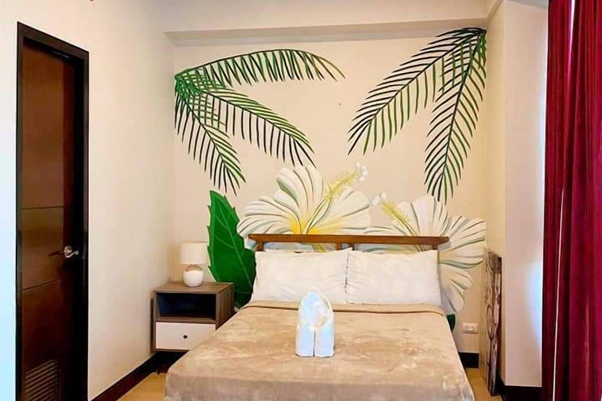 A bedroom with a bed, a nightstand, a large potted plant, and a door.