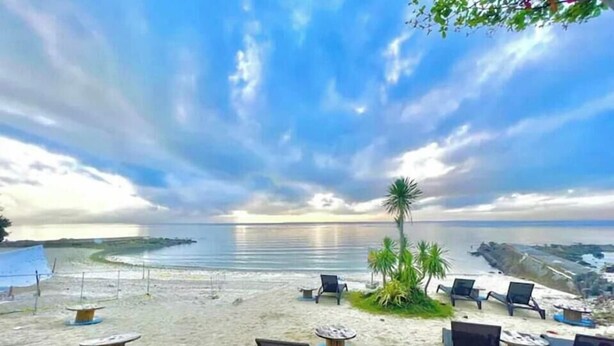 A beach with lounge chairs and tables, palm trees, and a view of the ocean. - The Mactan Newtown (Lapu-Lapu)