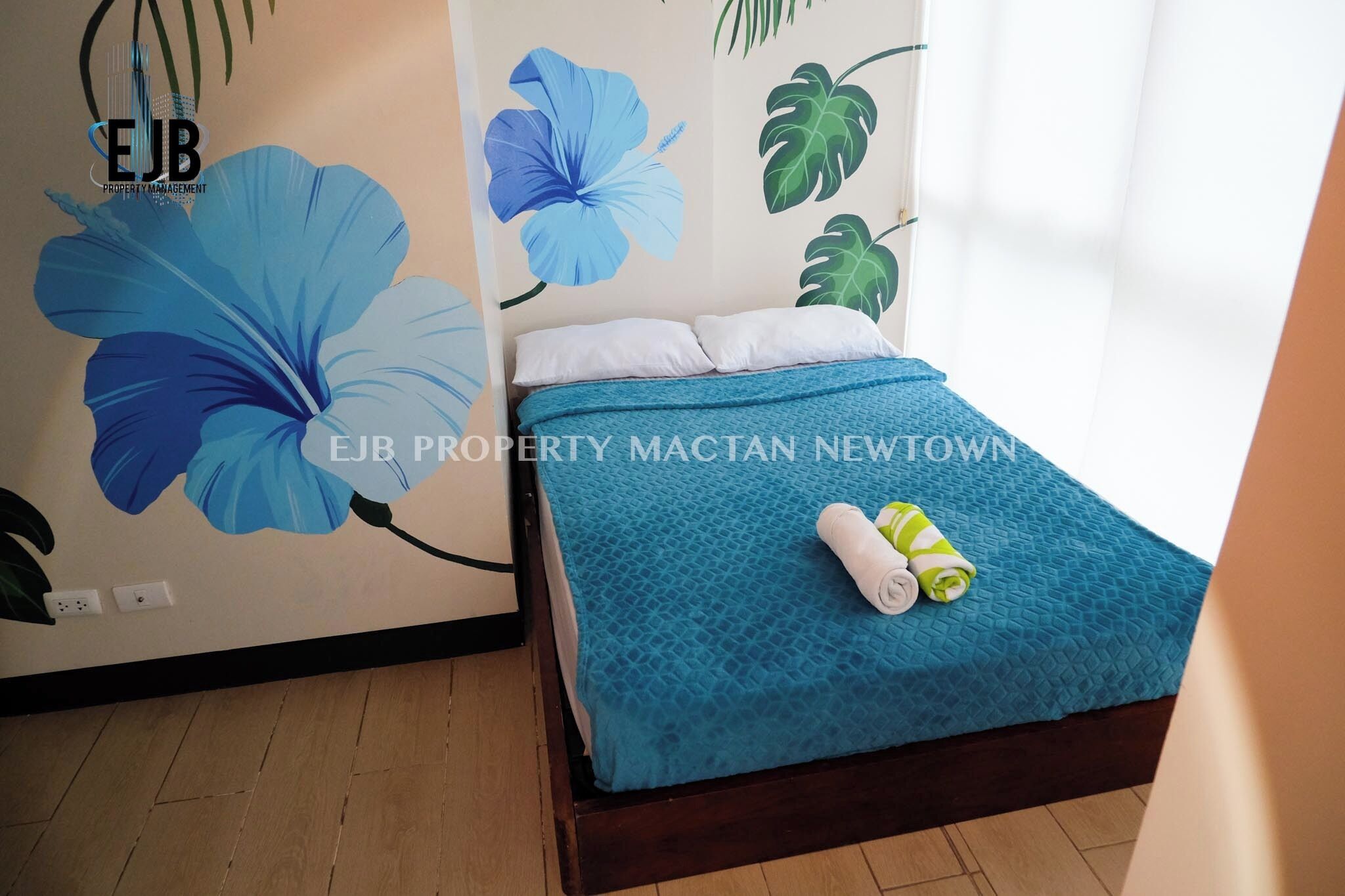 Un dormitorio con cama, ropa de cama azul y un mural de flores grandes.