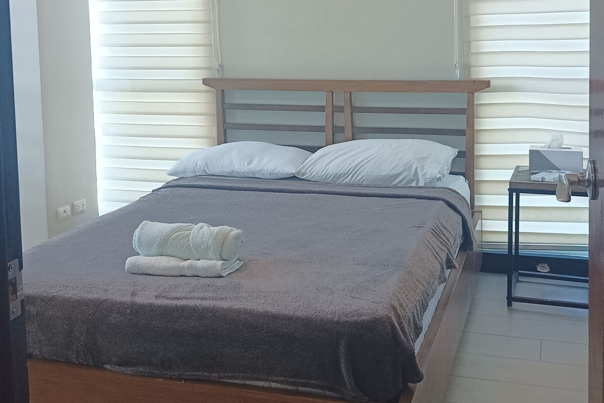 A bedroom with a bed, two bedside tables, and a window with blinds.