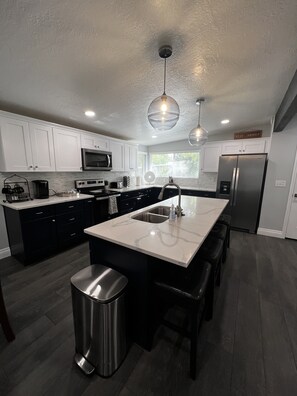 A modern kitchen with white cabinets, stainless steel appliances, and a marble island. - Cozy home centrally located  (West Valley City)
