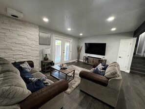 A modern living room with a sectional sofa, a coffee table, a flat-screen TV, and a stone wall. - Cozy home centrally located  (West Valley City)