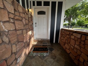 A stone exterior wall, a white door with a black trim, and a doormat with the text "oh happy day". - Cozy home centrally located  (West Valley City)