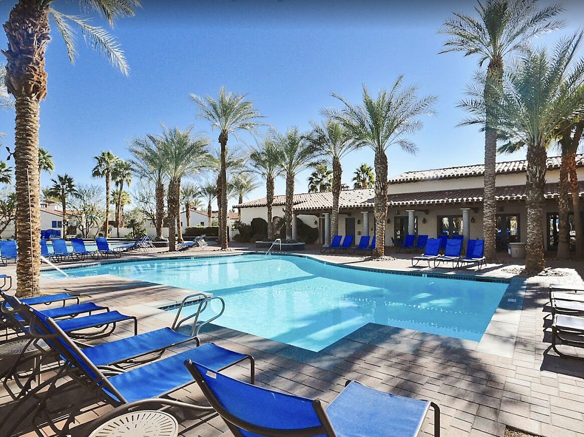 A pool area with blue lounge chairs and palm trees.