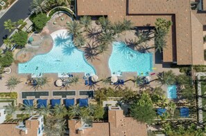 Ett flygbildsfoto av ett semesterområde med två pooler omgivna av palmer, solstolar och ett litet vattenfall.