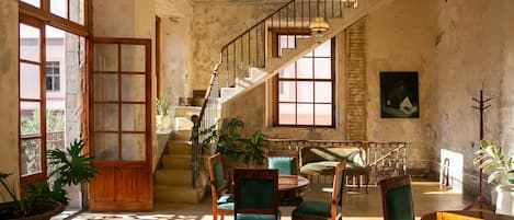 Una habitación amplia con escalera, sillas de madera, una mesa de comedor y ventanas grandes.