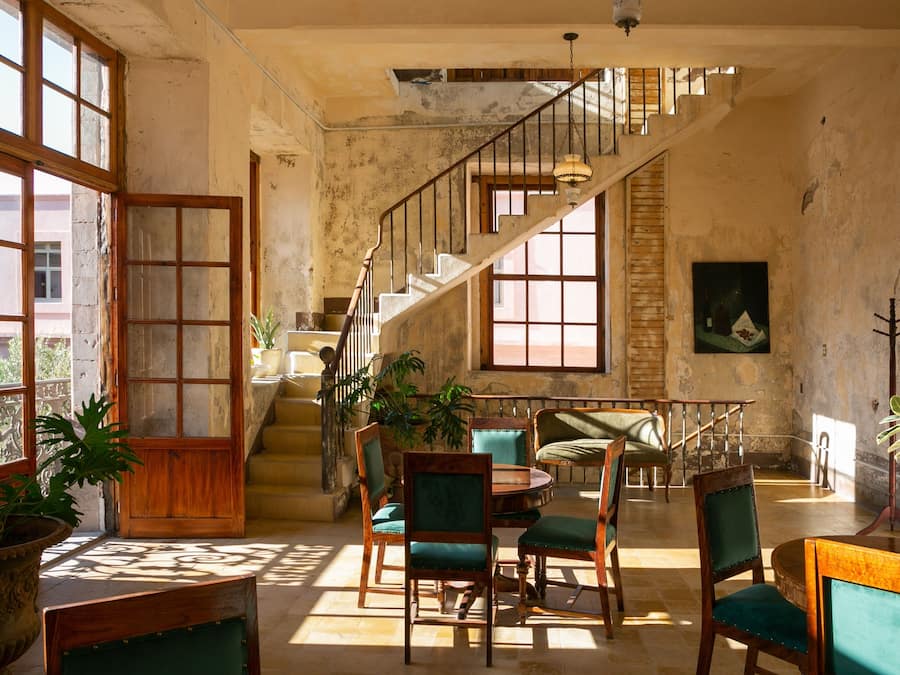 A spacious room with a staircase, wooden chairs, a dining table, and large windows.