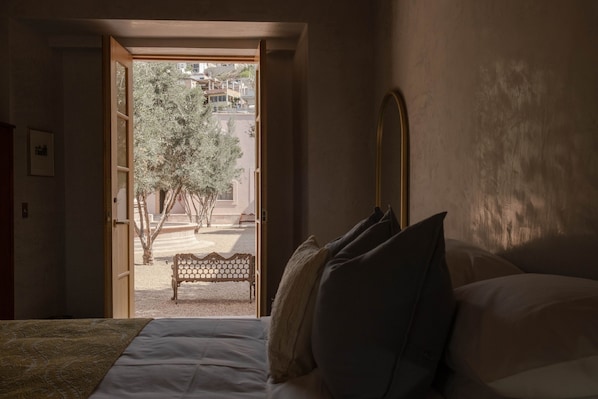 A bedroom with a bed, pillows, and a view of an outdoor area with a bench and trees. - Hotel Hércules (Querétaro)