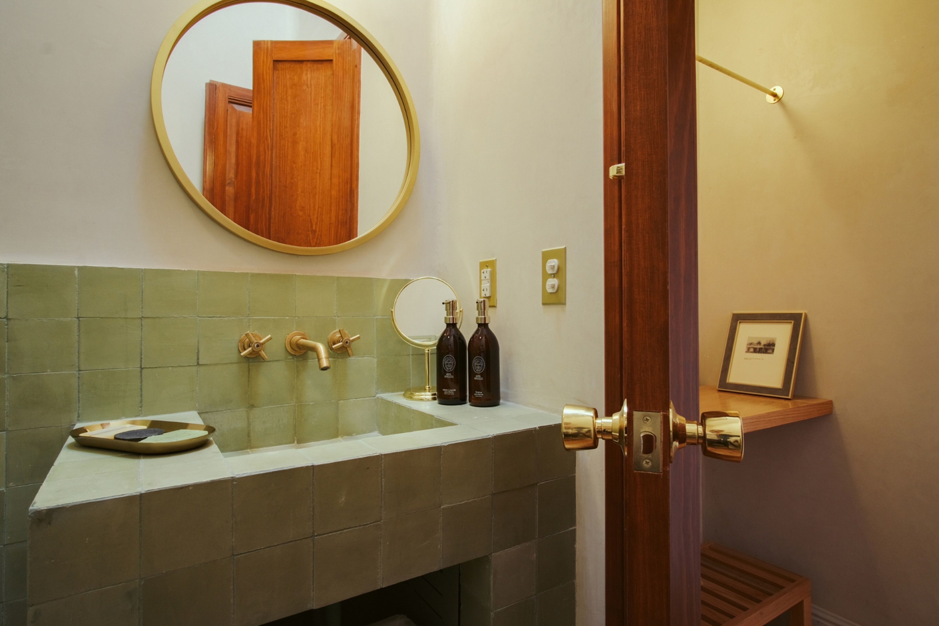 A bathroom with a round mirror, a sink, two bottles, and a framed picture on a shelf.