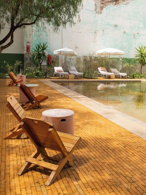 A poolside area with lounge chairs and umbrellas, a brick floor, and a wall with peeling paint. - Hotel Hércules (Querétaro)