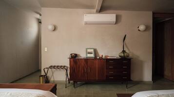 A hotel room with a bed, a wooden dresser, an air conditioner, and a small table.