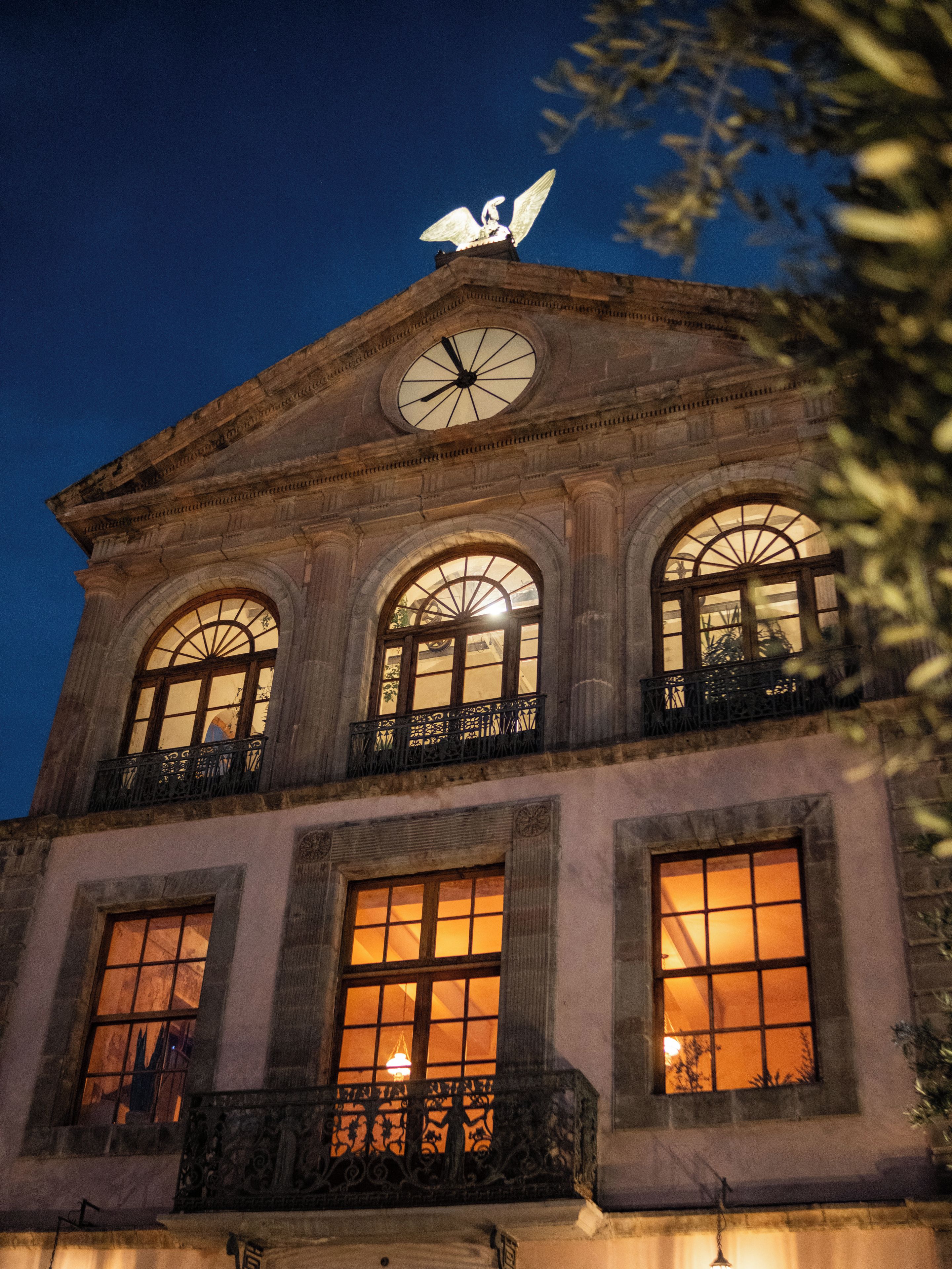 Un edificio histórico con una torre de reloj, ventanas arqueadas y un balcón con barandillas ornamentales.