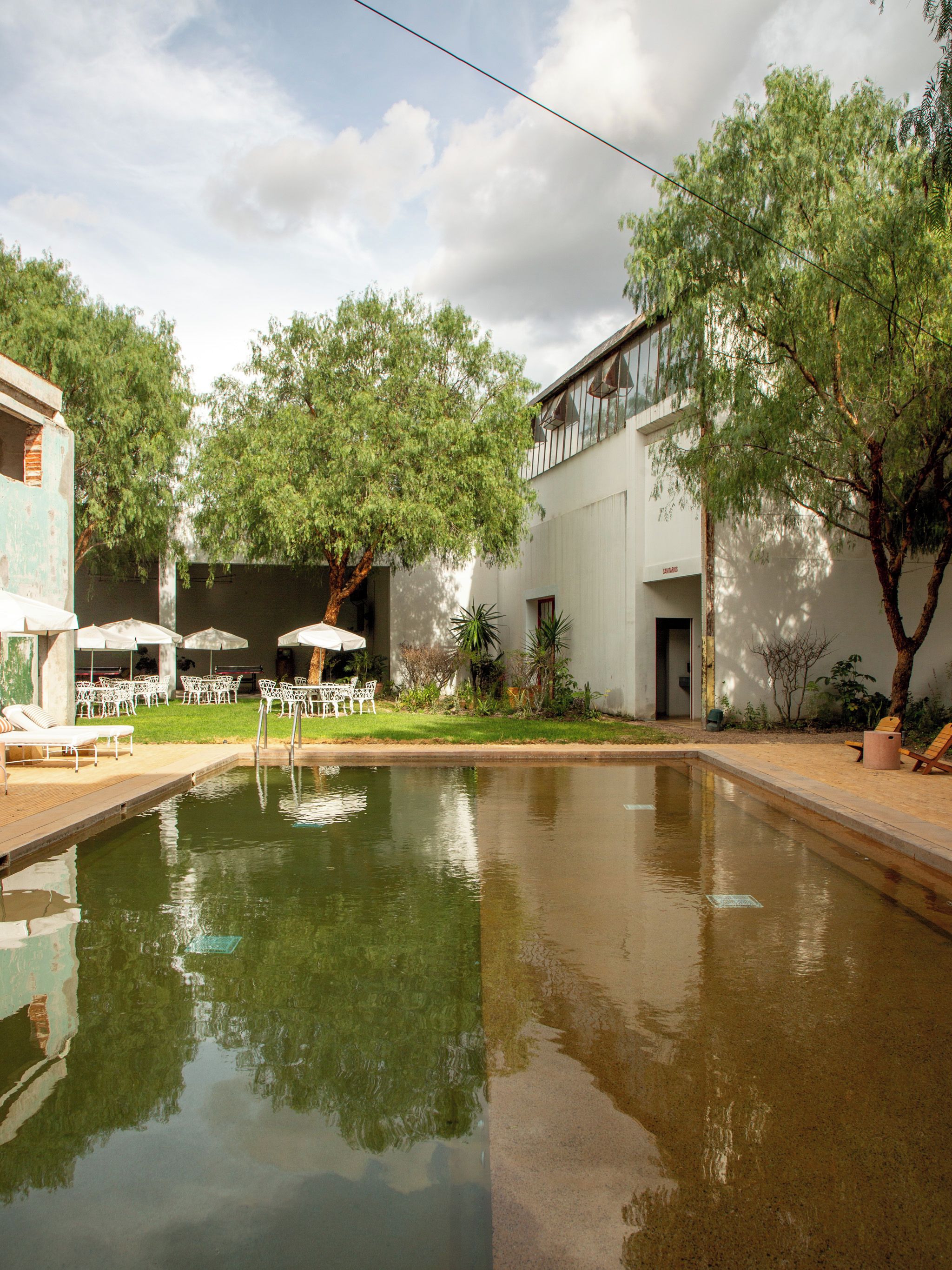 Un patio tranquilo con un estanque reflectante, mobiliario exterior y abundante vegetación.