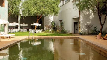 Un patio tranquilo con un estanque reflectante, mobiliario exterior y abundante vegetación.