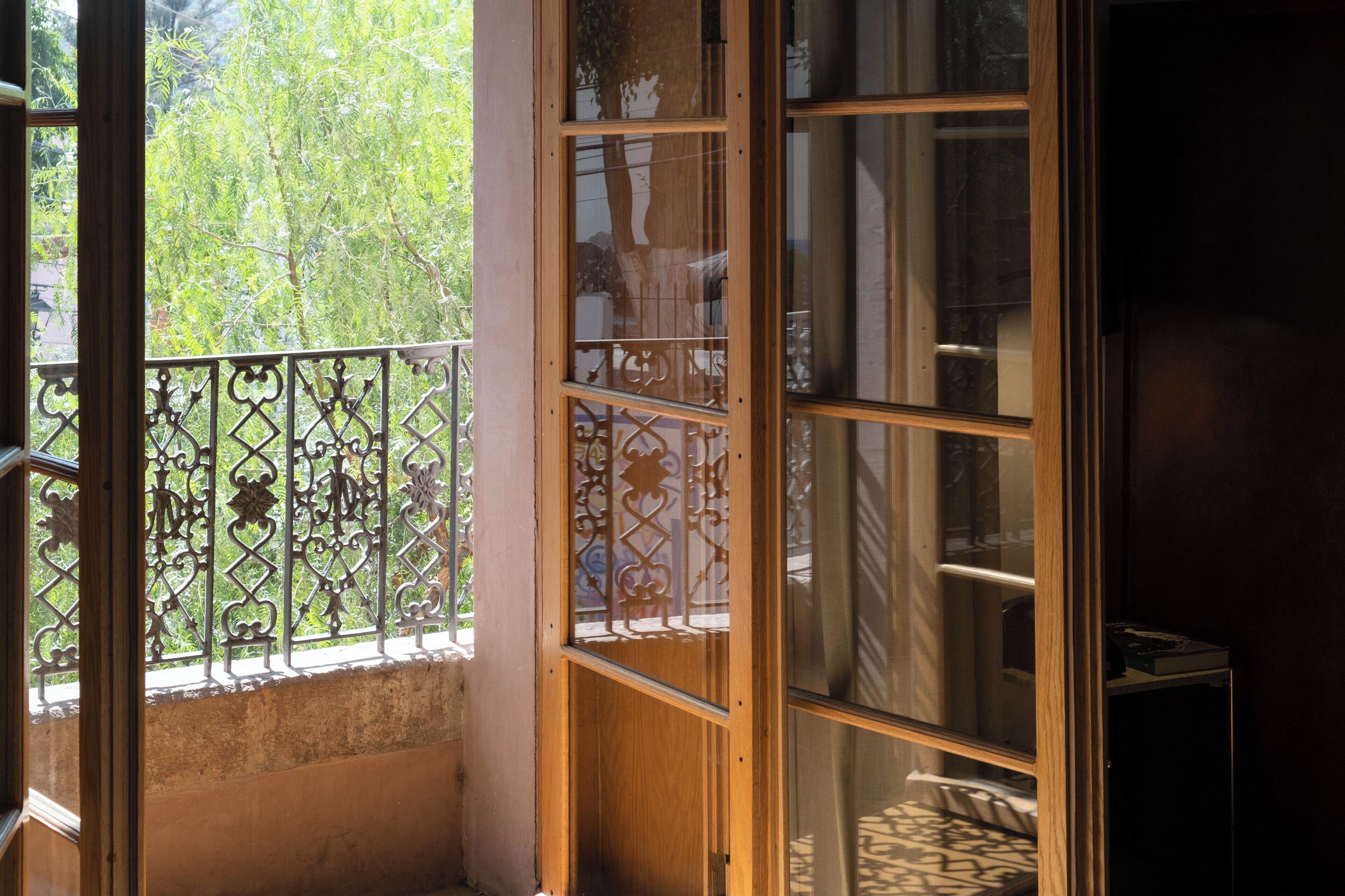 A room with a large window, a wooden door, and a metal balcony railing.