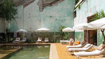 A swimming pool with lounge chairs and umbrellas, surrounded by a brick wall with peeling paint.