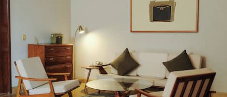 Un salon comprenant un canapé, deux fauteuils, une table basse, une lampe, une table d’appoint et un tableau encadré accroché au mur.