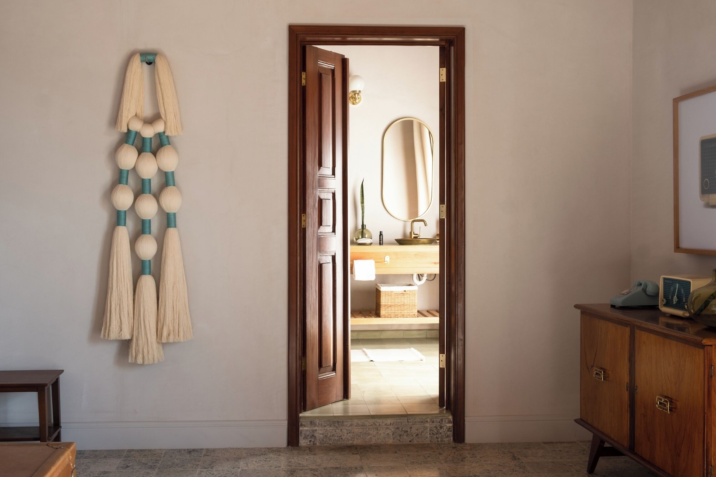 Un pasillo con una puerta de madera que da a un baño. Se observa un adorno de madera en la pared izquierda y un armario de madera a la derecha.