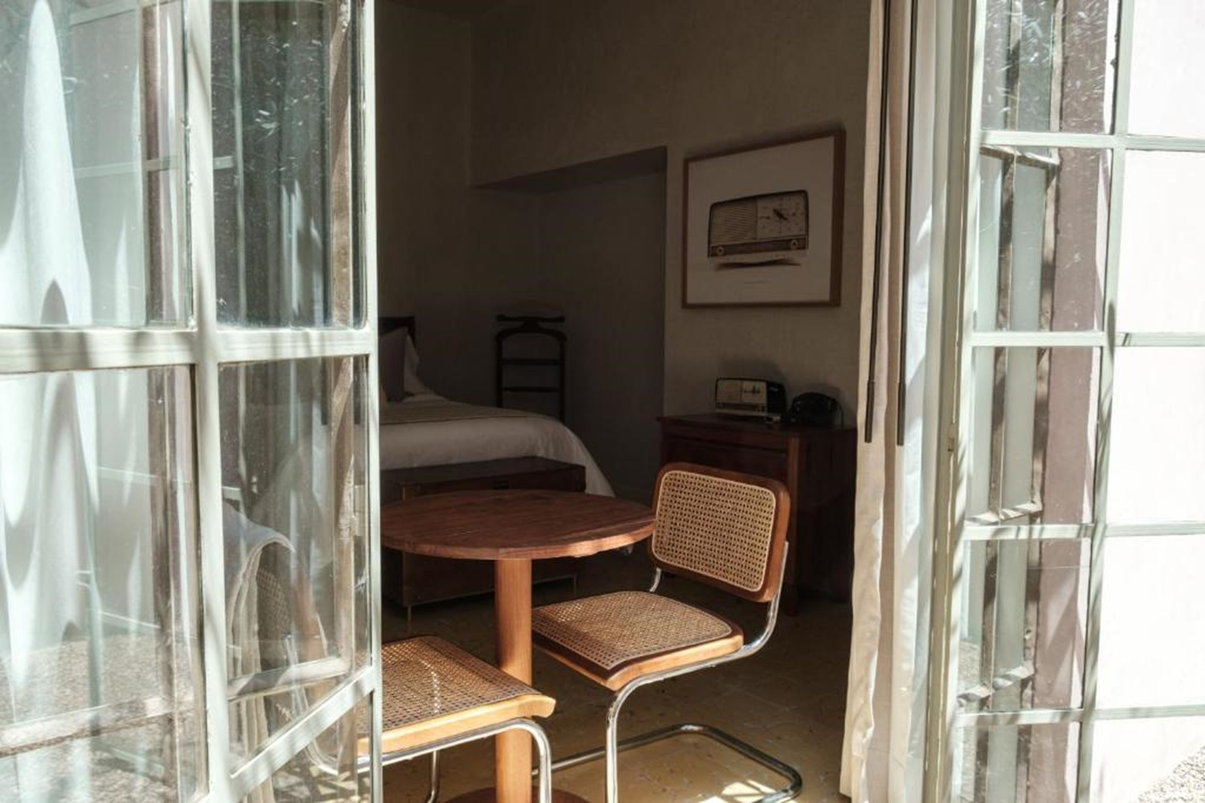 Una habitación con una cama, una mesa y una silla. Se ve una escalera apoyada en la pared y un cuadro enmarcado sobre la cama.