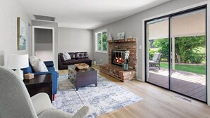 Ein modernes Wohnzimmer mit Kamin, einer Couch, einem Couchtisch und Blick auf einen Garten durch große Schiebetüren.