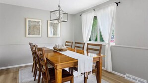 Ein Esszimmer mit Holztisch, Stühlen, einer Chandelierleuchtre und gerahmten Kunstwerken an der Wand.