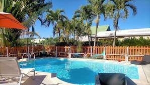 A swimming pool with lounge chairs and a wooden fence. - Topaze Orientale Équipé Pour 2 Personnes Discret Sans Vis-à-vis! Vue sur Jardin! (Sainte-Rose)